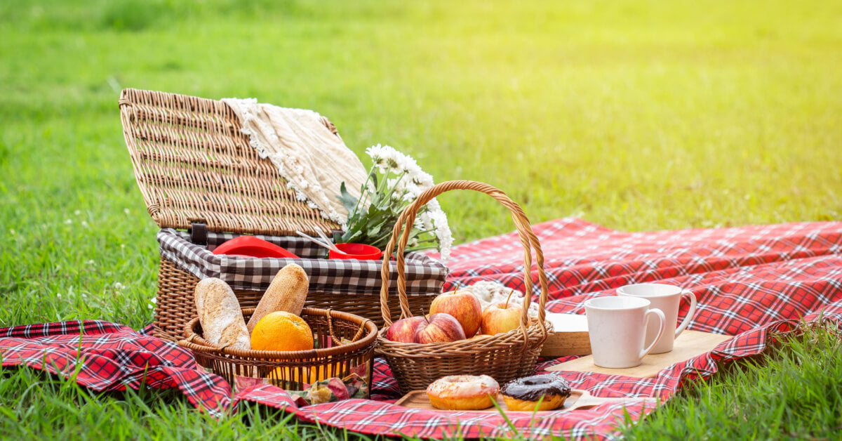 Picnic basket with fruit and bakery on red cloth in garden.