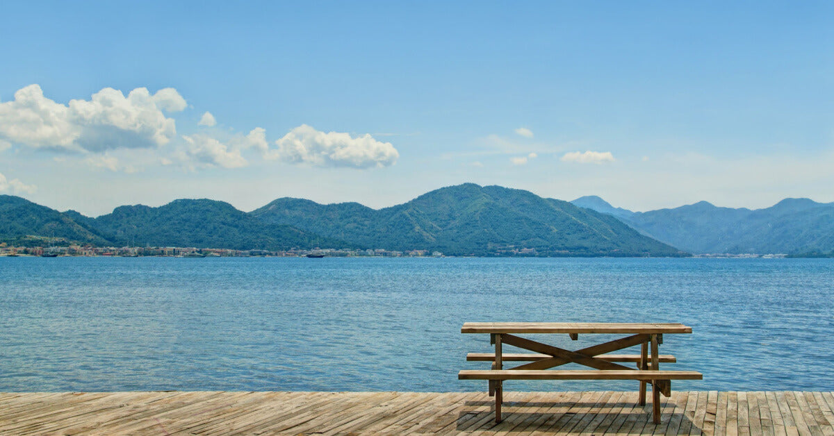 wooden table and two benches for picnic standing on wooden flooring by sea on sunny day facing green mountainous islands near Marmaris, Turkey